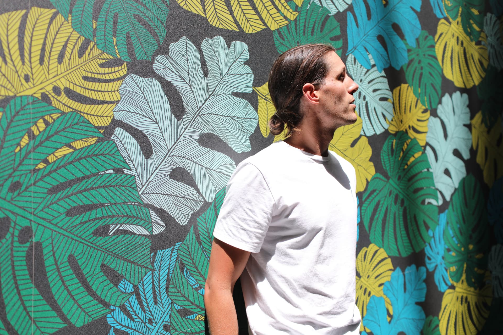 Sean in profile in front of a painted tropical leaf wall