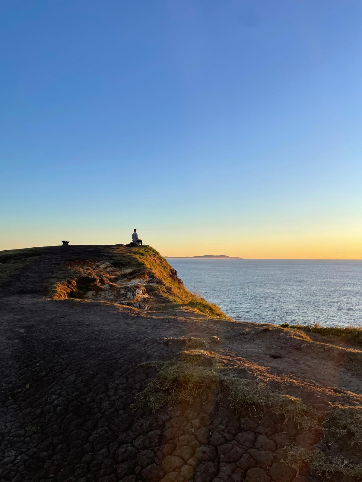 Sean Vitorovic sitting alone on a headland at Crescent Head, watching the sun come up over the ocean